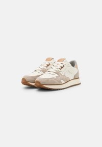 Paire de baskets en daim beige et cuir blanc avec lacets blancs et semelles en gomme sur fond blanc.