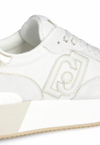 Weißer Schnürsneaker mit Obermaterial aus Mesh und Wildleder, mit einem glänzenden weißen Logo, beigen Akzenten und einer strukturierten Gummisohle.