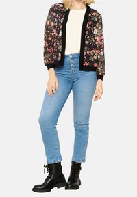 Blommig bomberjacka med svart kant, genomskinligt tyg och elastiska muddar, kombinerad med ljusblå högmidjade jeans och svarta snörstövlar.