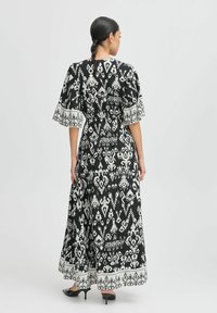 Maxi-Kleid in Schwarz und Weiß mit fließenden Ärmeln. Verfügt über komplexe Muster und einen kontrastierenden Saum. Hergestellt aus leichtem Stoff.
