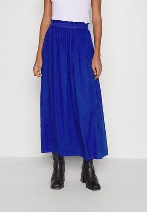 Blaue Maxirock mit gesammeltem elastischem Bund, fließendem Stoff und einfarbigem Design. Kombiniert mit schwarzen Stiefeln mit Absatz.