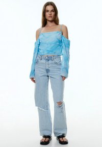 Blauwe marmeren sheer top met gelaagde ruffles, gecombineerd met lichtblauwe versleten wide-leg jeans en zwarte platform sandalen.
