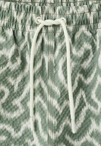 Tissu à motifs verts et blancs avec un cordon blanc passé à travers des œillets métalliques sur une ceinture froncée.