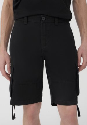 Pantaloni cargo neri realizzati in tessuto misto cotone. Tra le caratteristiche ci sono tasche laterali, orli con cordino e chiusura a bottone in vita.