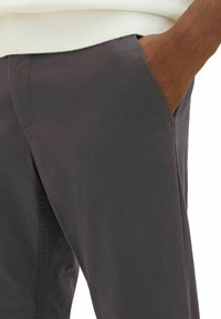 Grau melierte Baumwollmischungshosen mit slim Fit, seitlichen Taschen und sichtbaren Nähten. Der Stoff hat eine glatte Textur.