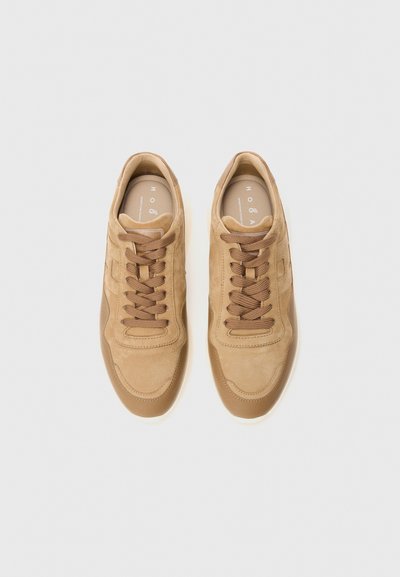 Un paio di sneakers in suede beige con lacci abbinati viste dall'alto su uno sfondo bianco semplice.
