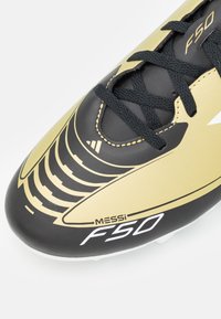 Scarpa da calcio nera e dorata con motivi intricati, dotata di materiale superiore testurizzato, lacci neri e suola bianca con tacchetti.