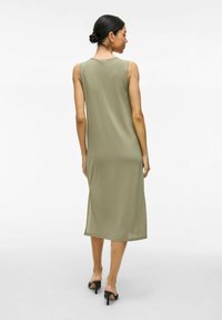 Sukienka bez rękawów w oliwkowym kolorze o prostym fasonie, do kolan, gładkiej teksturze i okrągłym dekolcie. Noszona z czarnymi sandałami na obcasie.