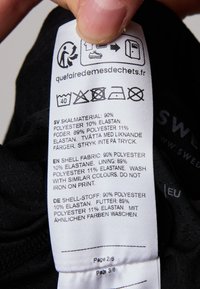 Svart tvättlapp med tvättsymboler, material: 90% polyester, 10% elastan; tryckt på flera språk med återvinningsikon.