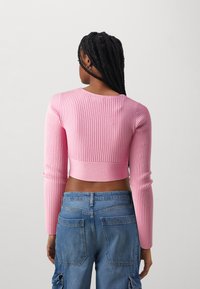 Rosa gerippter Crop-Top mit langen Ärmeln, das ein enges Design und einen runden Ausschnitt aufweist. Kombiniert mit blauen Denim-Cargohosen.