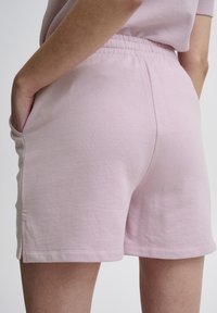 Světle růžové bavlněné kraťasy s elastickým pasem, postranními kapsami a úzkým lemem. Tkanina má hladký a jemný povrch.