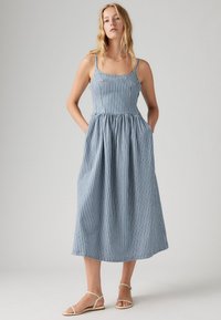 Μπλε και λευκή ριγέ βαμβακερή midi φόρεμα με εφαρμοστό κορσέ, τετράγωνη λαιμόκοψη και φούστα με ζάξεις. Ρυθμιζόμενοι ιμάντες και πλάγιες τσέπες.