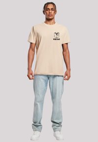 Beige cotton t-shirt featuring a black graphic of an open book and the text "WISE DAD" on the left chest. Worn with light blue jeans and white sneakers.