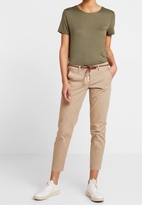 Olivgrön kortärmad t-shirt, beige skräddarsydda byxor, flätat brunt bälte och vita sneakers; minimalistisk design med en slät yta.