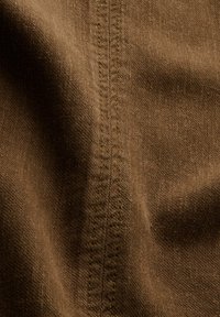 Close-up of brown fabric with detailed double stitching down the center, highlighting texture and seam structure.