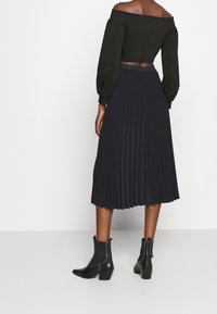 Top corto nero con spalle scoperte e maniche a sbuffo abbinato a una gonna midi plissettata di un blu navy scuro e stivaletti con tacco basso.