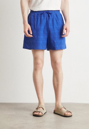 Blaue strukturierte Badeshorts mit einem elastischen Bund und Kordelzug. Kombiniert mit sandfarbenen Sandalen mit einem Doppelriemen-Design.
