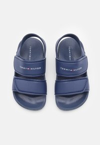Granatowe sandały z dwiema regulowanymi paskami. Wykonane z gładkiego materiału z białym logo Tommy Hilfiger. Płaska podeszwa z minimalną teksturą.