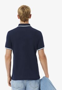 Polo de color azul marino con un cuello estructurado y detalles en azul claro, con mangas cortas y textura lisa. Llevado con unos vaqueros de denim azul claro.