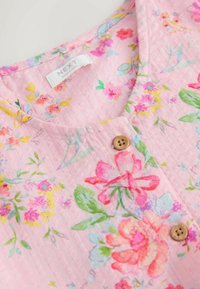 Tela rosa claro con patrones florales en varios colores, con un escote redondo y un botón de madera. La etiqueta dice "NEXT".