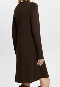 Brun långärmad stickad klänning med avslappnad passform, med ribbade ärmslut och fåll, slät textur och knälång längd.