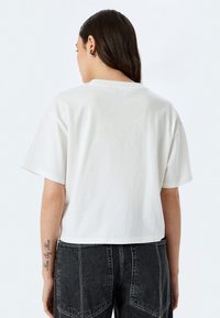 Camiseta blanca recortada con mangas cortas, diseño limpio, hecha de una tela suave. Combinada con pantalones de mezclilla oscuros de talle alto.
