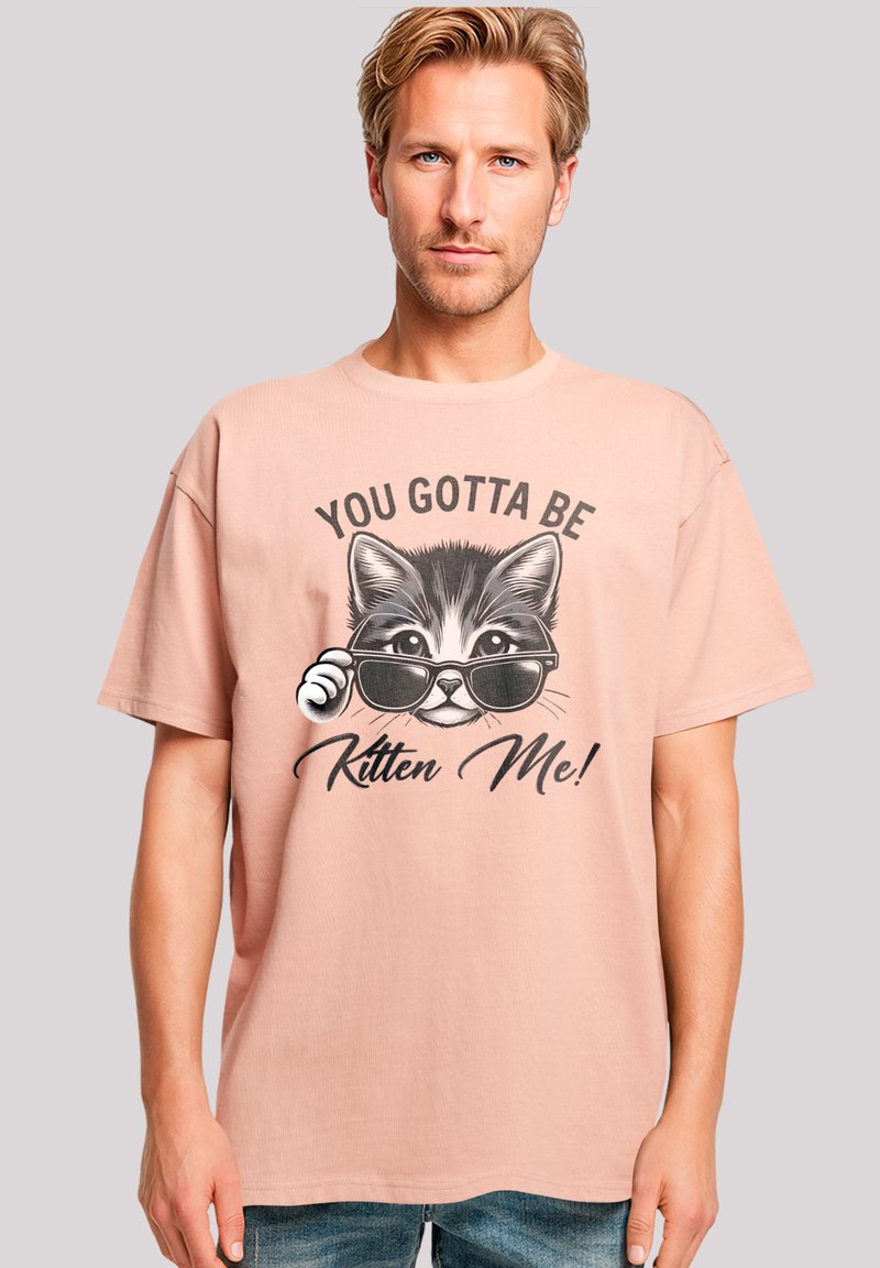 Light pink cotton t-shirt features a graphic design of a cat wearing sunglasses with the text "YOU GOTTA BE KITTEN ME!" in bold black lettering.