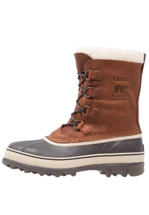 Brązowy i czarny ocieplany trzewik zimowy z wiązaniem z przodu, grubą podeszwą i białym futrem, oznaczony jako "Caribou Sorel Waterproof."