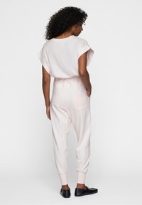 Helles rosa Jumpsuit mit kurzen Ärmeln, tapered Beinen und gerippten Bündchen; verfügt über eine Rückentasche und eine glatte Textur. Trägt man mit schwarzen Ballerinas.
