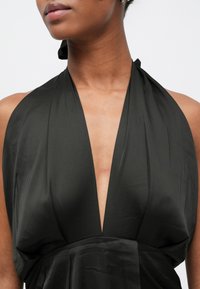 Schwarzes Neckholderkleid mit tiefem V-Ausschnitt, aus glattem, glänzendem Stoff mit weicher Textur, das elegant an der Taille fällt.