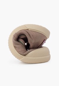 Tenis de pânză maro, cu o structură moale și flexibilă, talpă din cauciuc beigie și o etichetă brodată, evidențiind un design rotund și răsucit.