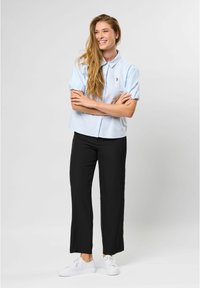 Light blue short-sleeve button-up shirt with a small emblem, paired with black wide-leg pants and white sneakers.