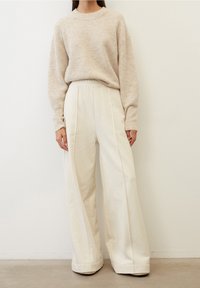 Suéter de punto beige con mangas largas combinado con pantalones de pierna ancha color crema, que presentan una cintura alta y costuras laterales. Textura suave, ajuste casual.