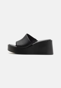 Sandales à talons compensés en cuir noir avec un dessus lisse et un talon plateforme, présentant un design minimaliste et une finition légèrement texturée.