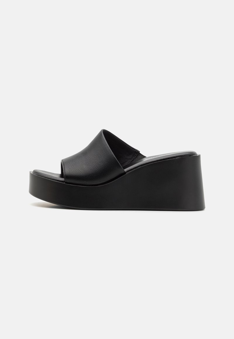 Sandales à talons compensés en cuir noir avec un dessus lisse et un talon plateforme, présentant un design minimaliste et une finition légèrement textur�ée.