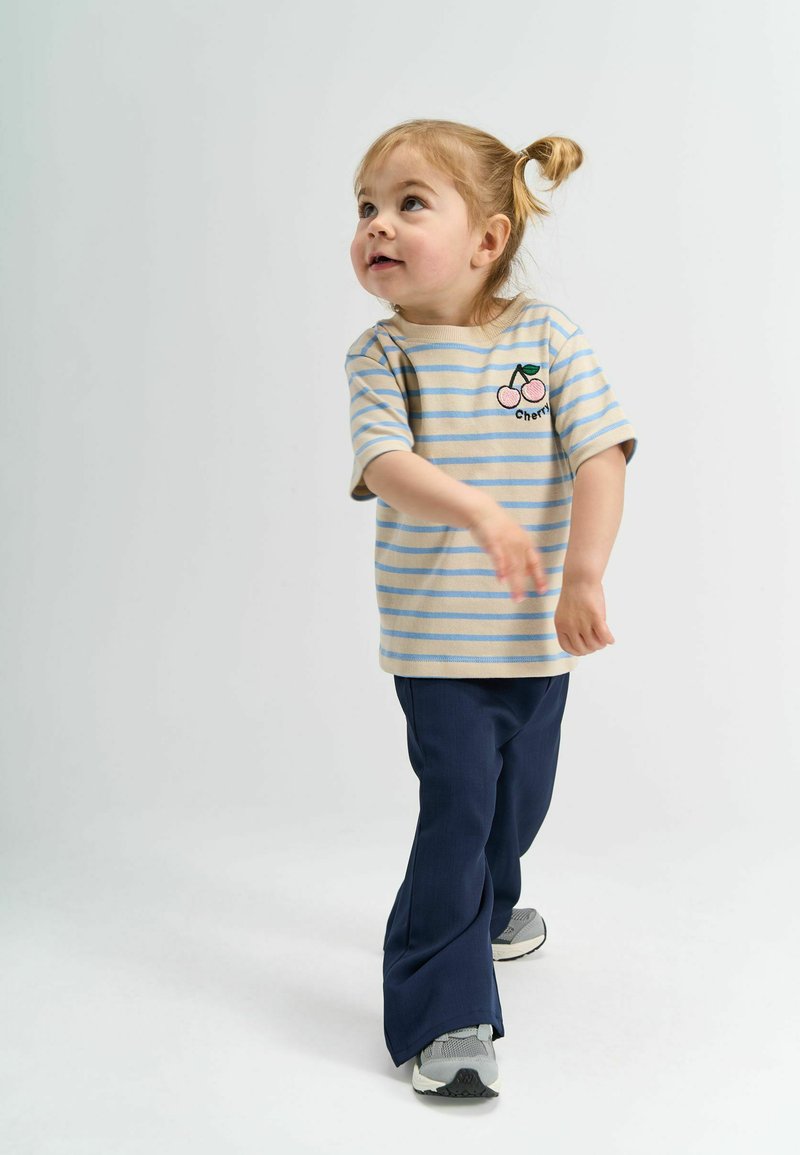 Prúžkované béžové a svetlomodré tričko s vyšitou čerešňou, skombinované s námorníckymi rozšírenými nohavicami a sivými teniskami.