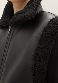 Schwarze Lederweste mit einem strukturierten schwarzen Kunstpelzkragen. Verfügt über einen vorderen Reißverschluss und glattes Gewebe, das einen Kontrast zur Weichheit des Kragens bildet.