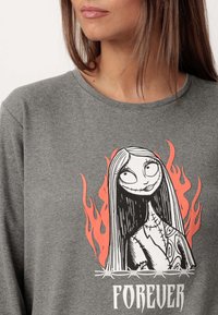Camisa de manga larga gris con un estampado gráfico de una mujer con cabello negro y características de esqueleto, rodeada de llamas naranjas y la palabra "FOREVER."
