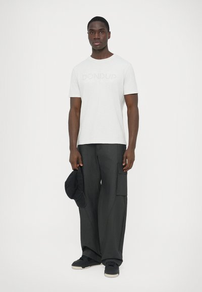 T-shirt blanc à manches courtes avec logo "DON DUP", associée à un pantalon cargo noir ample et une casquette noire, avec une coupe oversize et un tissu texturé.