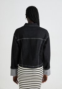 Black denim jacket with contrasting white stitching, featuring a classic collar and cropped design. Paired with a striped ribbed skirt.