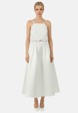 Woman wearing a sleeveless white midi dress with floral lace bodice, spaghetti straps, cutout detail at waist, and pleated satin skirt.