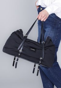 Zwarte nylon sporttas met leren accenten, gestructureerde vorm, dubbele handgrepen bovenaan en zilveren hardware. Bevat een minimaal logo-opdruk.
