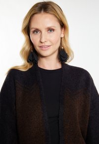 Cardigan lavorato a maglia in marrone scuro e blu navy con un design strutturato. Orecchini lunghi neri e un top nero completano il look.