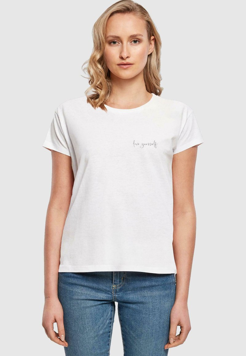 Tricou din bumbac alb cu mâneci scurte, decolteu rotund, având un mic imprimeu "trăiește-te pe tine" în gri pe partea stângă.