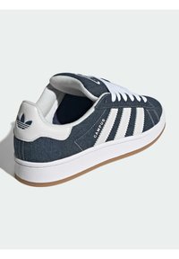 Siniset farkkukengät valkoisilla yksityiskohdilla, joissa on kolme raitaa, valkoinen kumipohja ja pehmustettu kaulus. Adidas-logo kantapäässä.