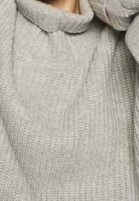 Pull gris clair avec un motif de tricot texturé, doté d'un col montant et d'une coupe décontractée. Matière douce avec un aspect cosy.