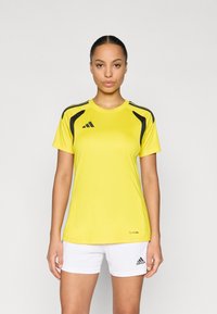 Κίτρινο αθλητικό μπλουζάκι με μαύρες λεπτομέρειες, κοντά μανίκια και στρογγυλή λαιμόκοψη. Συνδυάζεται με λευκά σορτς με μαύρο λογότυπο.