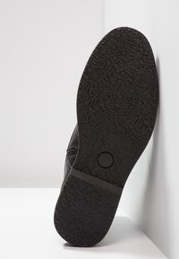 Suola di scarpa nera con motivo di grip testurizzato, cerniera laterale visibile e marcatura di dimensione 42, posizionata su uno sfondo bianco.