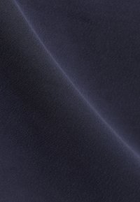 Gros plan sur un tissu bleu foncé avec une texture lisse, étroitement tissée, et des plis doux créant des ombres délicates.