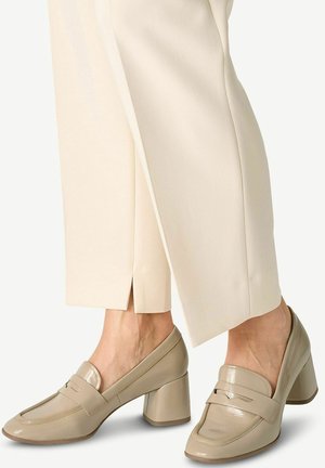 Beige leather block-heeled loafers with a glossy finish, featuring a raised seam and a rounded toe. Paired with cream-colored trousers.